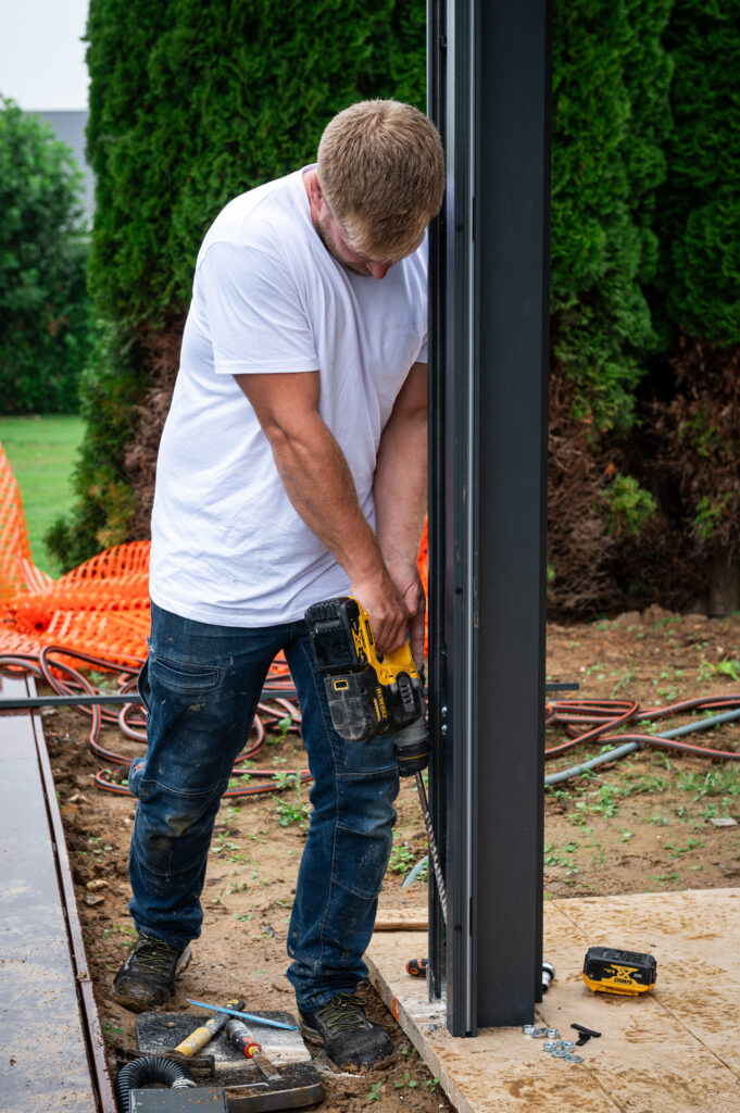 homme avec un perforateur au niveau d'un poteau de pergola bioclimatique